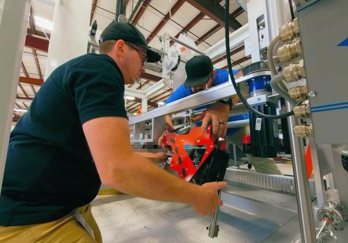 Two workers install a red component on an industrial pharmaceutical machine in a manufacturing facility.