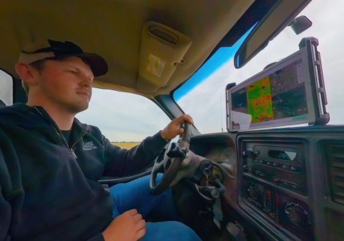 An agronomist drives a truck through a field of crops while monitoring a digital map on a tablet mounted to the dashboard.
